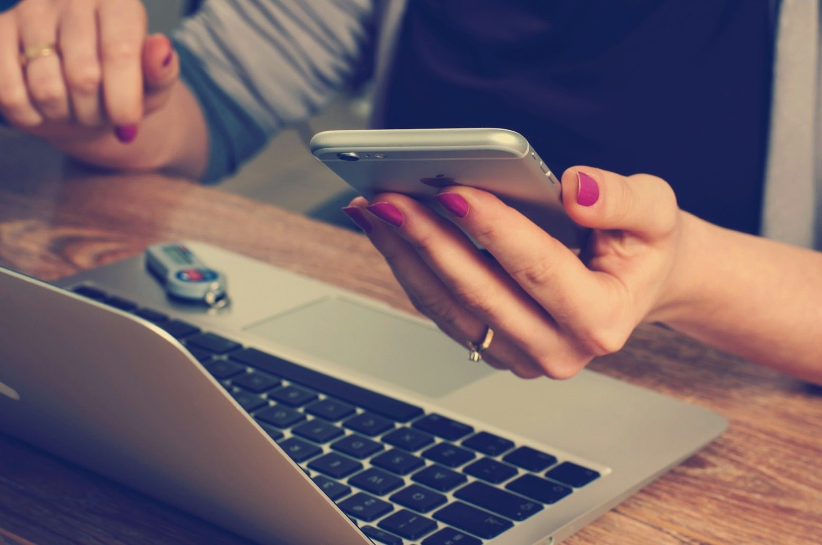 Person using a phone at a desk with a laptop
